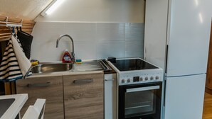 A compact kitchen with a sink, stove, oven, and a refrigerator. - 'Courseulles Comme À La Maison' Apartment with Private Terrace and Wi-Fi (Courseulles-sur-Mer)