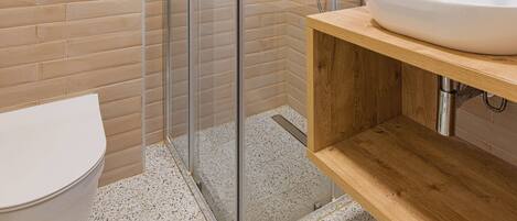 A modern bathroom with a glass-enclosed shower, a white toilet, and a wooden vanity with a sink.