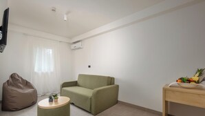 A minimalist living room with a green sofa, a round coffee table, a bean bag, and a fruit bowl on a wooden side table. - Hotel Delfin (Omišalj)