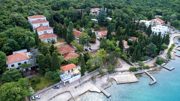 An aerial view of a coastal residential area with houses, a dock, and a swimming area. - Hotel Delfin (Omišalj)