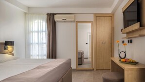 A hotel room with a bed, a desk with a fruit bowl, a TV, and a wardrobe. - Hotel Delfin (Omišalj)