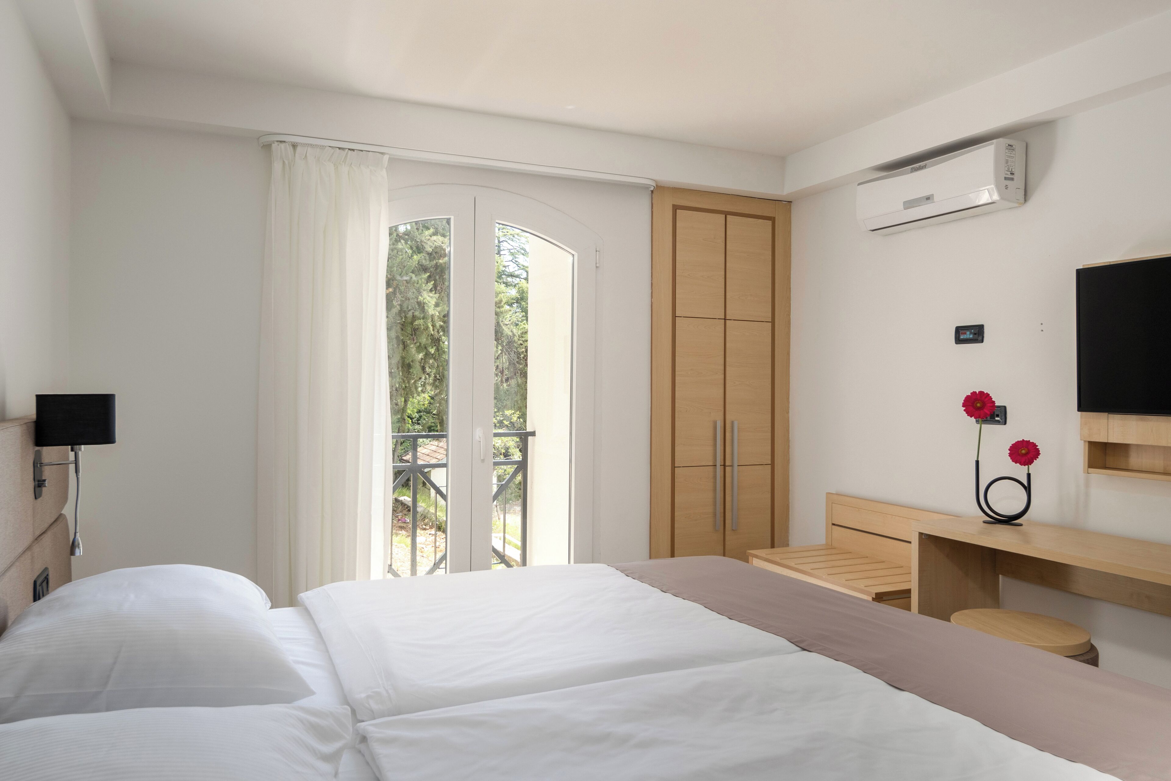A hotel room with a bed, a desk, a TV, and an air conditioning unit.
