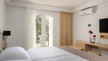 A hotel room with a bed, a desk, a TV, and an air conditioning unit.
