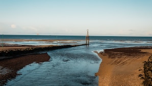 A coastal landscape with a sandy beach, a rocky outcrop, and a pier extending into the water. - La Voile de Nacre – Ground Floor Apt, 50m from Beach, Bernières-sur-Mer (Bernières-sur-Mer)