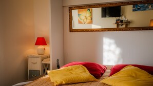 A bedroom with a bed, pillows, a bedside table with a lamp, a mirror, and a wall art piece. - La Voile de Nacre – Ground Floor Apt, 50m from Beach, Bernières-sur-Mer (Bernières-sur-Mer)