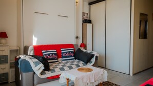 A cozy living room with a sofa, a small table, and a wardrobe. - La Voile de Nacre – Ground Floor Apt, 50m from Beach, Bernières-sur-Mer (Bernières-sur-Mer)