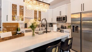 A modern kitchen with white cabinetry, stainless steel appliances, a chandelier, and a welcome sign. - Private Resort Stay - Insta-Worthy Miami Vacation (Miami)