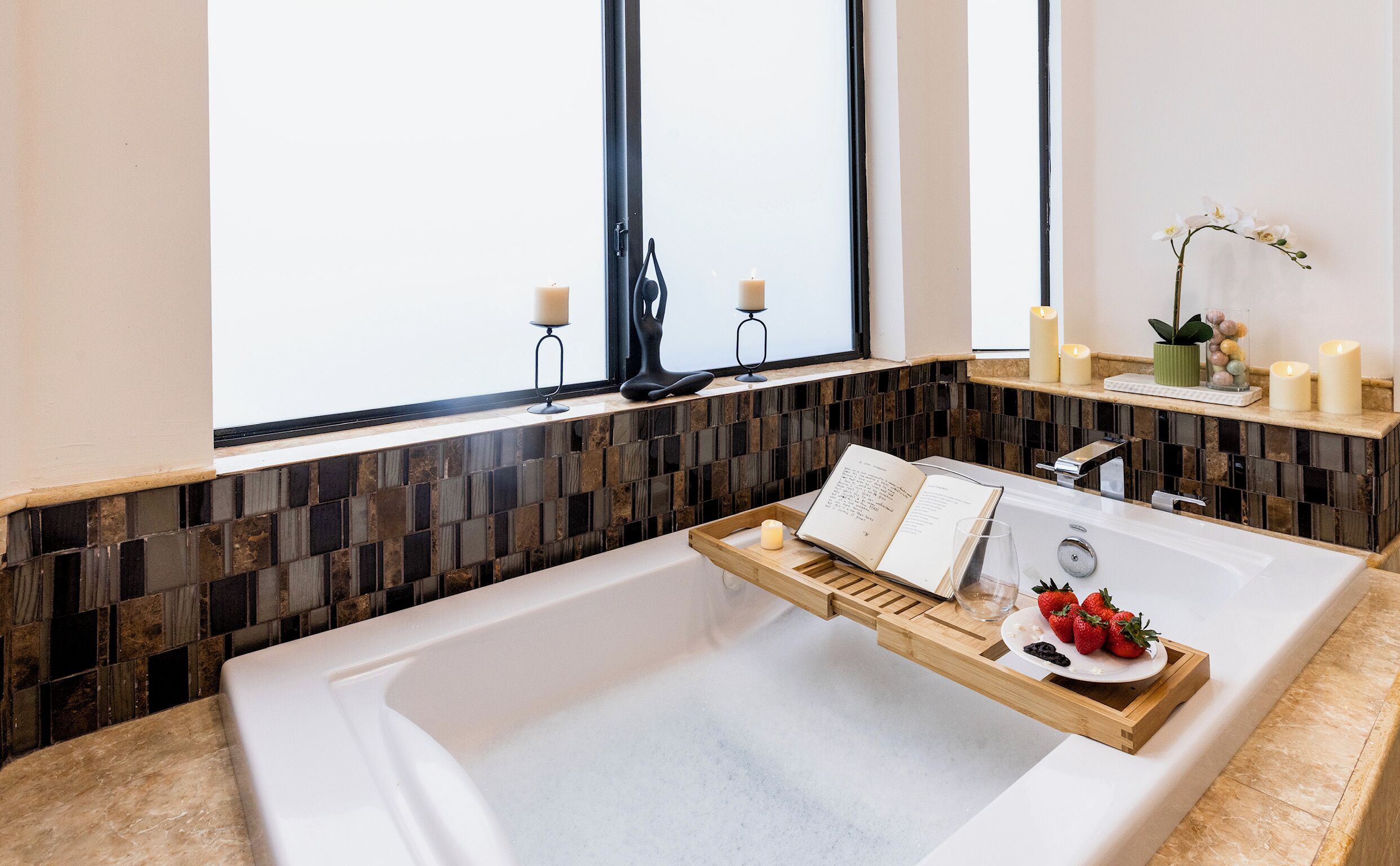 Une salle de bain moderne avec une grande baignoire, un meuble-lavabo avec un miroir et une fenêtre décorée de bougies.