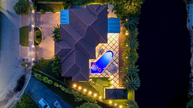 An aerial view of a property with a large geometric roof structure, a swimming pool, and a well-lit driveway. - Private Resort Stay - Insta-Worthy Miami Vacation (Miami)