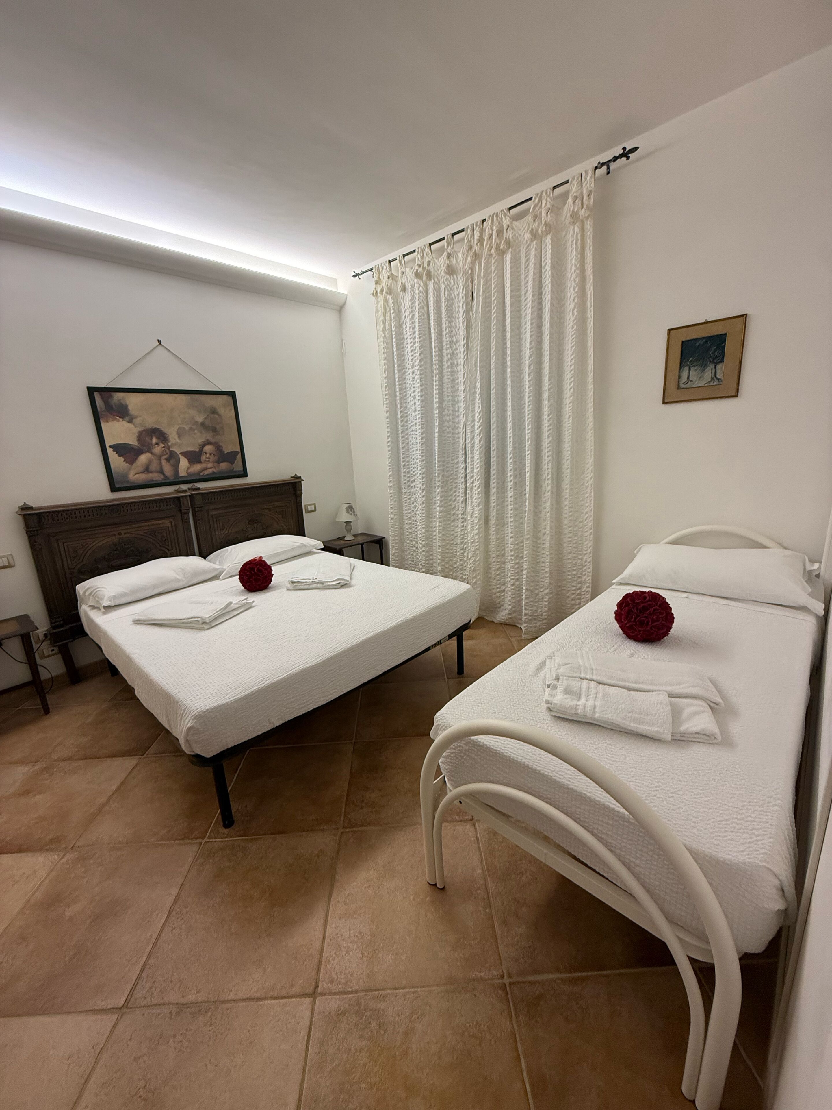 Ein Hotelzimmer mit zwei Betten, einem Nachttisch, einer Lampe, einem Gemälde und einem Vorhang.