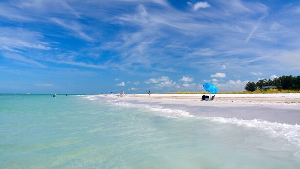 A beach with clear turquoise water, a sandy shore, and a few people and umbrellas. - Hidden Haven / Private Pool & Hot Tub (Holmes Beach)