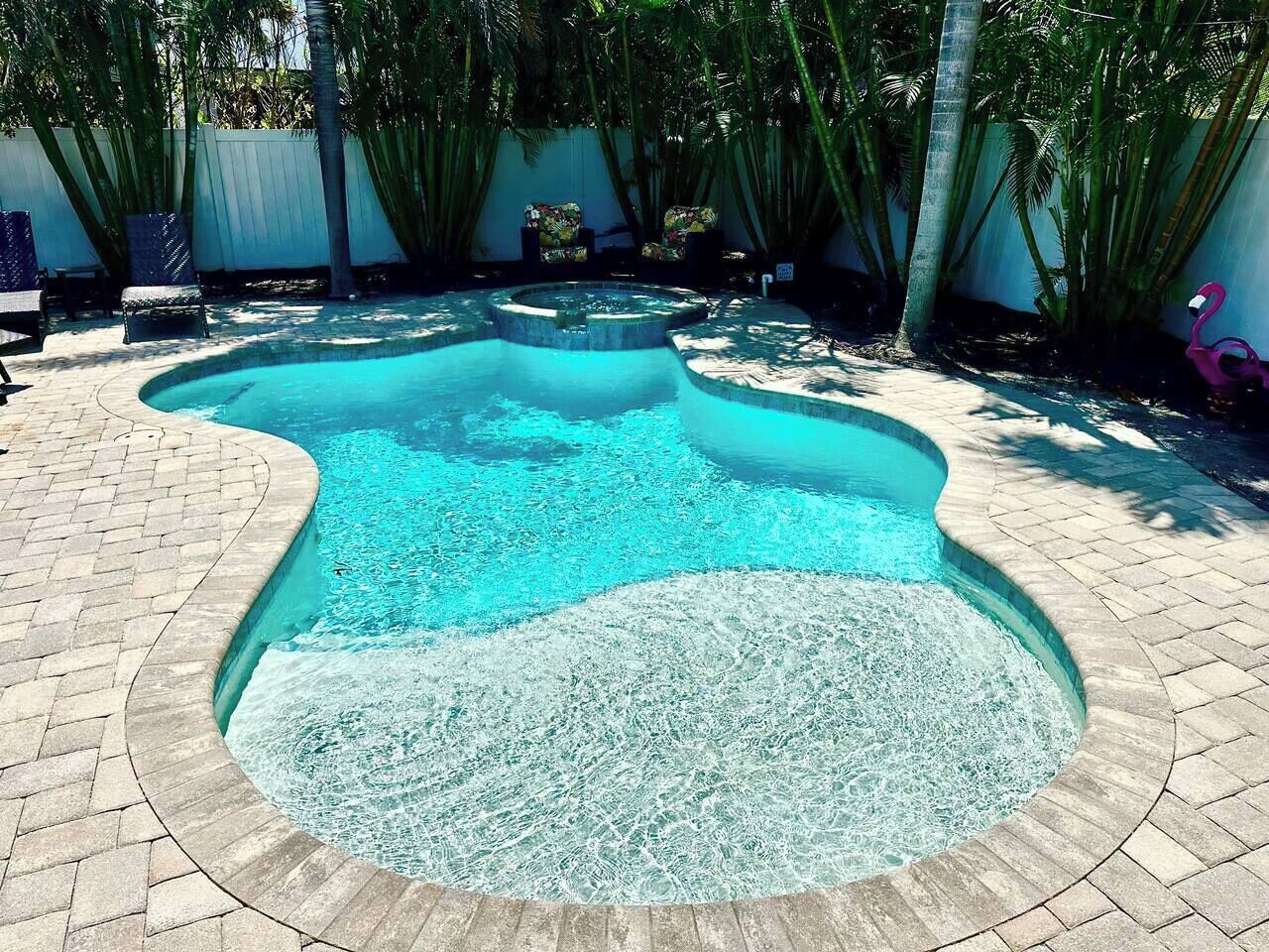 Ein Pool mit ungewöhnlicher Form, umgeben von einer Pflasterterrasse und Palmen.