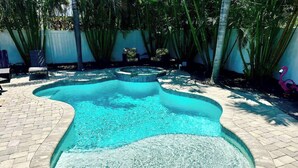 A swimming pool with a unique shape, surrounded by a brick patio and palm trees. - Hidden Haven / Private Pool & Hot Tub (Holmes Beach)