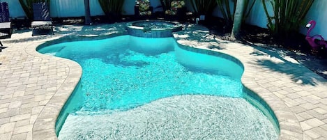 A swimming pool with a unique shape, surrounded by a brick patio and palm trees.