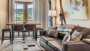 Una sala de estar acogedora con un sofá de cuero, una mesa de comedor con sillas y vistas a un bosque a través de amplios ventanales.