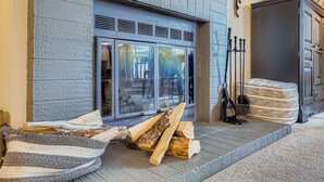 Una chimenea con leña, un sillón de mimbre y un armario.