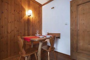 A wooden dining table with chairs, a red placemat, and wine glasses set for two.
