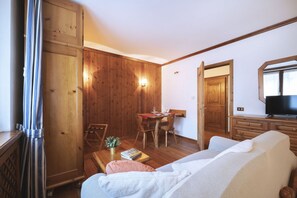 A cozy room with wooden walls, a dining area, a sofa, and a TV.