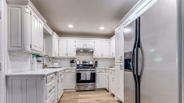 A modern kitchen with white cabinetry, a stainless steel refrigerator, and a wood floor. - Charming house in Fort Worth walking distance to TCU (Fort Worth)