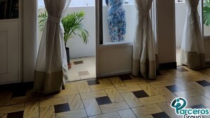 Une pièce dotée d’une grande porte-fenêtre coulissante, de rideaux blancs, d’un sol à motifs et offrant une vue sur les bâtiments environnants.