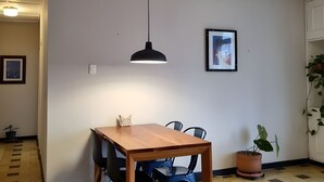 Une pièce avec une table en bois, des chaises bleues, un luminaire suspendu noir, un tableau encadré au mur et une plante en pot.