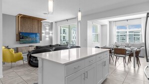 Une cuisine moderne dotée d’un îlot central, d’un coin repas avec des chaises et d’un téléviseur fixé au mur.