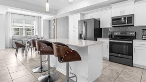 Une cuisine moderne avec des meubles blancs, des appareils en acier inoxydable et un îlot central doté de tabourets de bar.