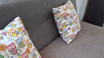 Un sofá gris con dos almohadones coloridos con diseños de búhos y flores.