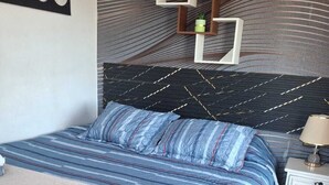 A bedroom with a bed, a nightstand, a wall-mounted shelf, and a wall art piece.