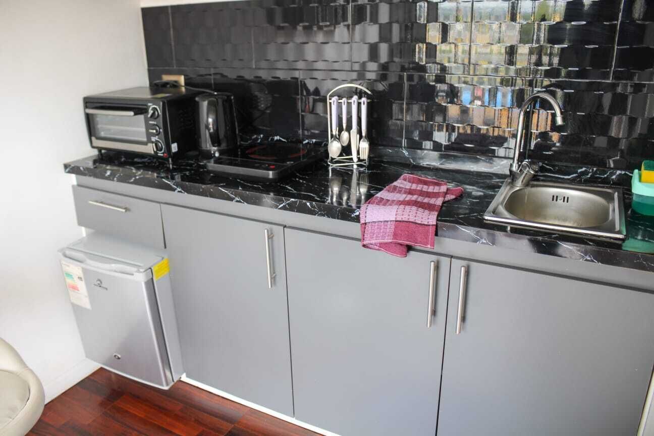 A kitchen with a black tiled backsplash, a stainless steel sink, a microwave, and a small refrigerator.