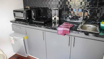 A kitchen with a black tiled backsplash, a stainless steel sink, a microwave, and a small refrigerator.