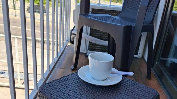 A balcony with wicker furniture, a white cup on a saucer, and a view of the street.