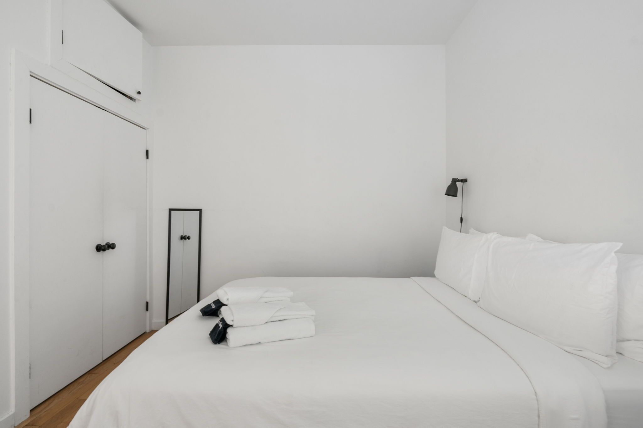 Una camera d'albergo dal design minimalista, con un letto rifatto, un armadio e una lampada da comodino.