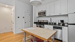 Una cocina moderna con gabinetes blancos, un microondas de acero inoxidable, una cafetera y un lavavajillas.