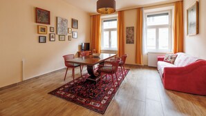 A dining area with a wooden table and red chairs, a red sofa, and a large window with curtains. - Jugendstil Boutique Studio, 57 m², original art, central family hotel (Wien)