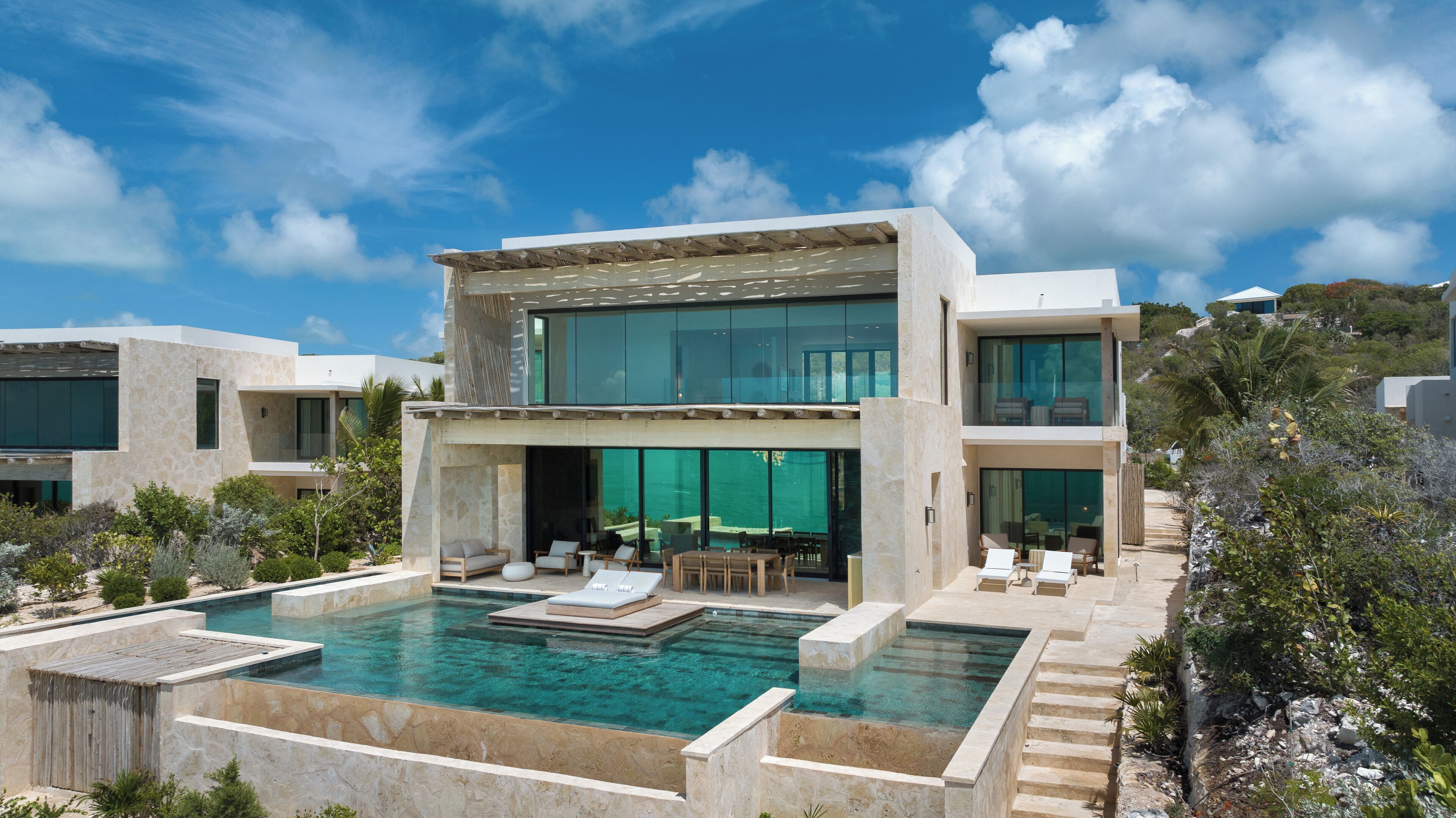 Una casa moderna de dos pisos con piscina, mobiliario exterior y vistas del paisaje circundante.
