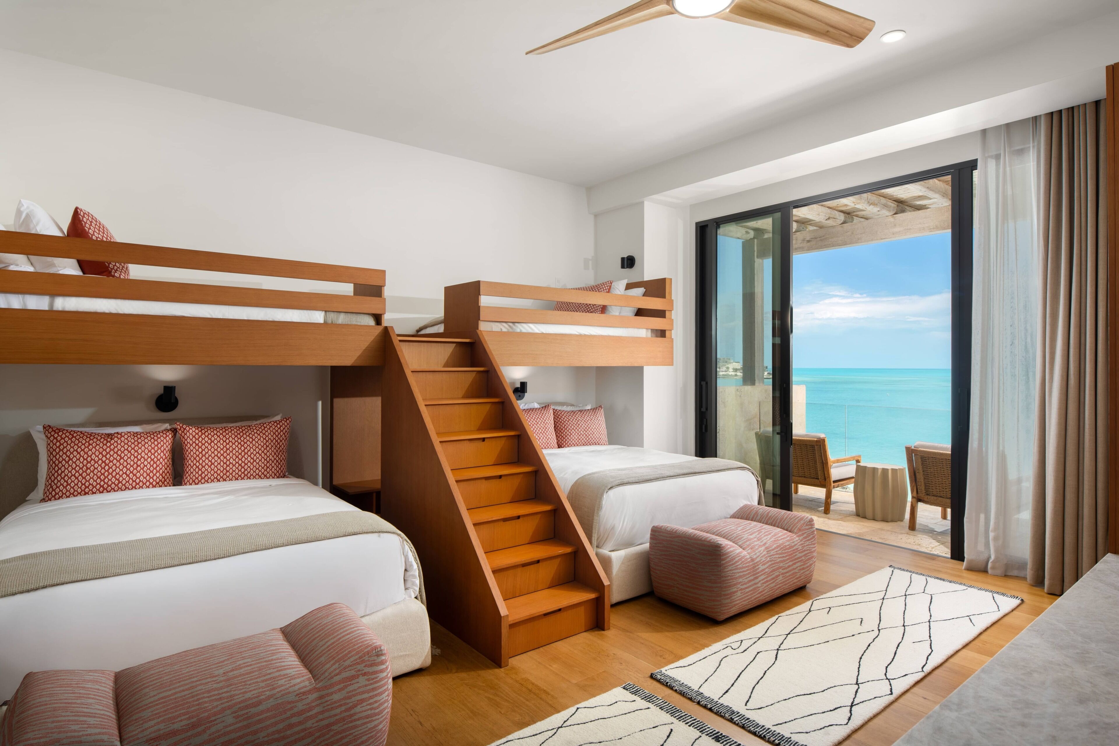 Une chambre d’hôtel moderne avec des lits superposés, un escalier, un balcon donnant sur la mer et un coin salon.