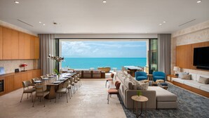A spacious living area with a large window overlooking the ocean, a dining area with a long table and chairs, and a seating area with sofas and a TV. - The Strand Turks and Caicos (Providenciales)