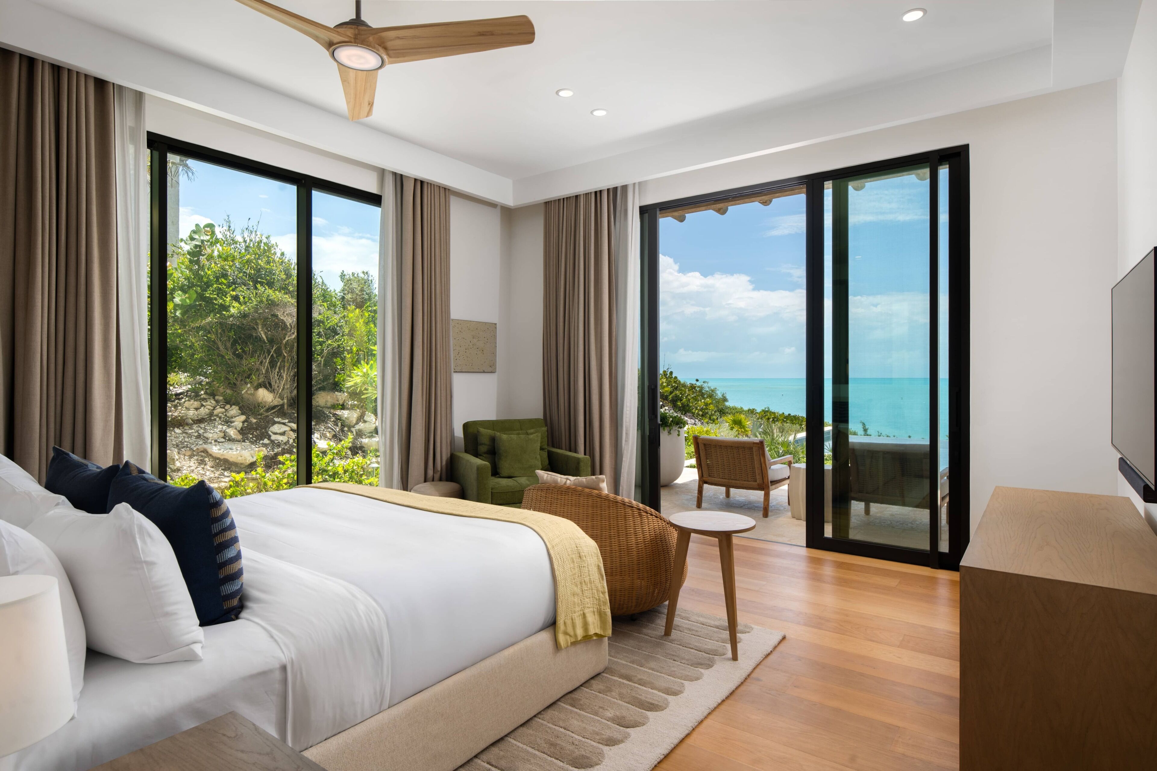 A modern hotel room with a large bed, a seating area, and a balcony with a view of the ocean.