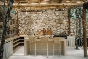 A stone wall with hanging lights, a stone bench, and a bar area with chairs. - Villa Najil Chak Tulum : 16 Guests : Private Pool : Groups Retreats & Events (Tulum)