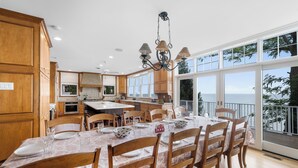 A spacious kitchen with wooden cabinets, a large dining table set for six, and a view of the sea through large windows. - New Buffalo Sandcastle (New Buffalo)