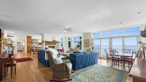 A spacious living room with a piano, a large blue sofa, a rocking chair, and a dining area with a table and chairs. - New Buffalo Sandcastle (New Buffalo)