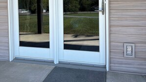A double glass door entrance with a doormat and a wall-mounted light fixture.