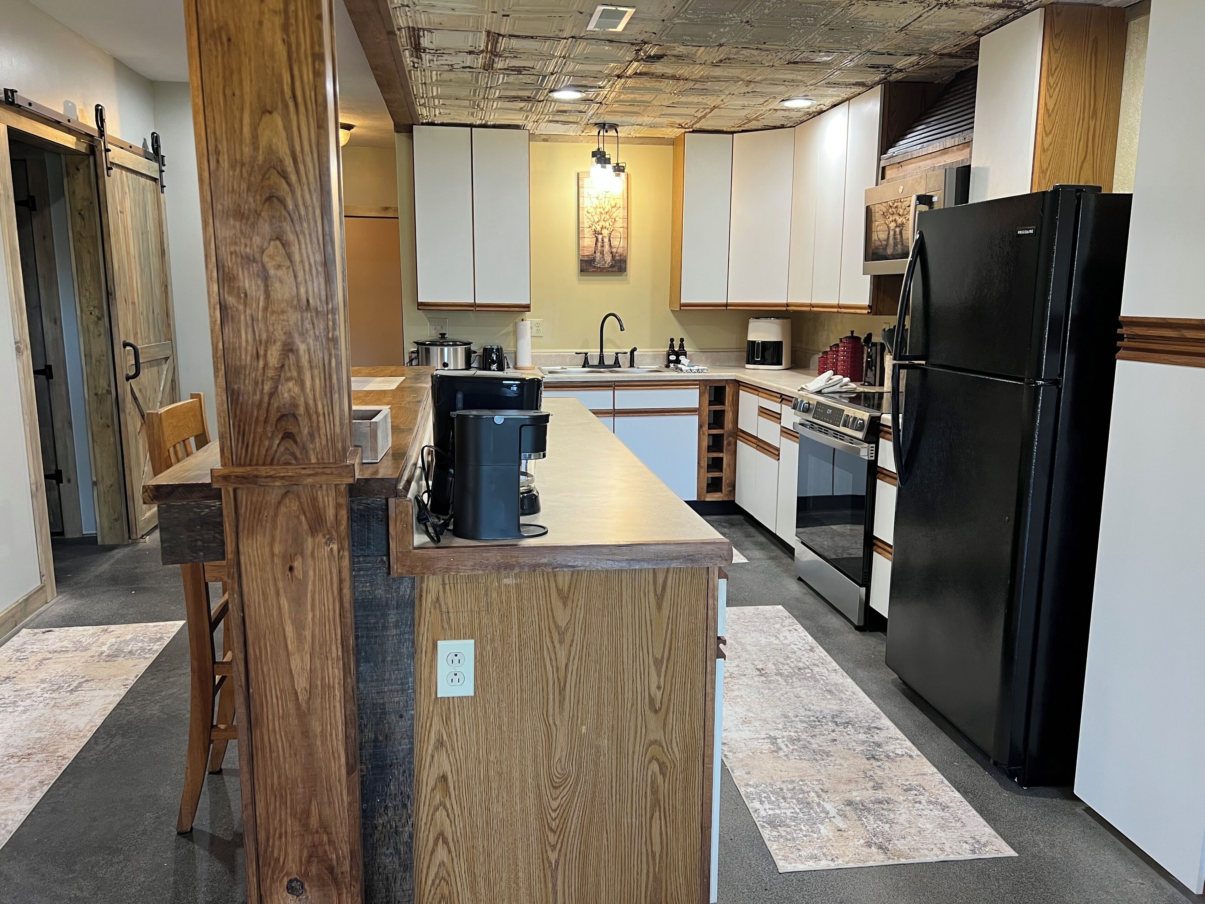 A kitchen with a central island, wooden cabinets, a black refrigerator, and a hanging light fixture.