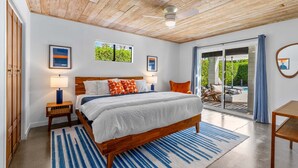 A bedroom with a wooden ceiling, a large bed, two bedside tables with lamps, a view through a glass door to an outdoor area, and framed artwork on the walls. - Sunny Dreams - Mid-Century Pool & Spa Retreat (Palm Springs)