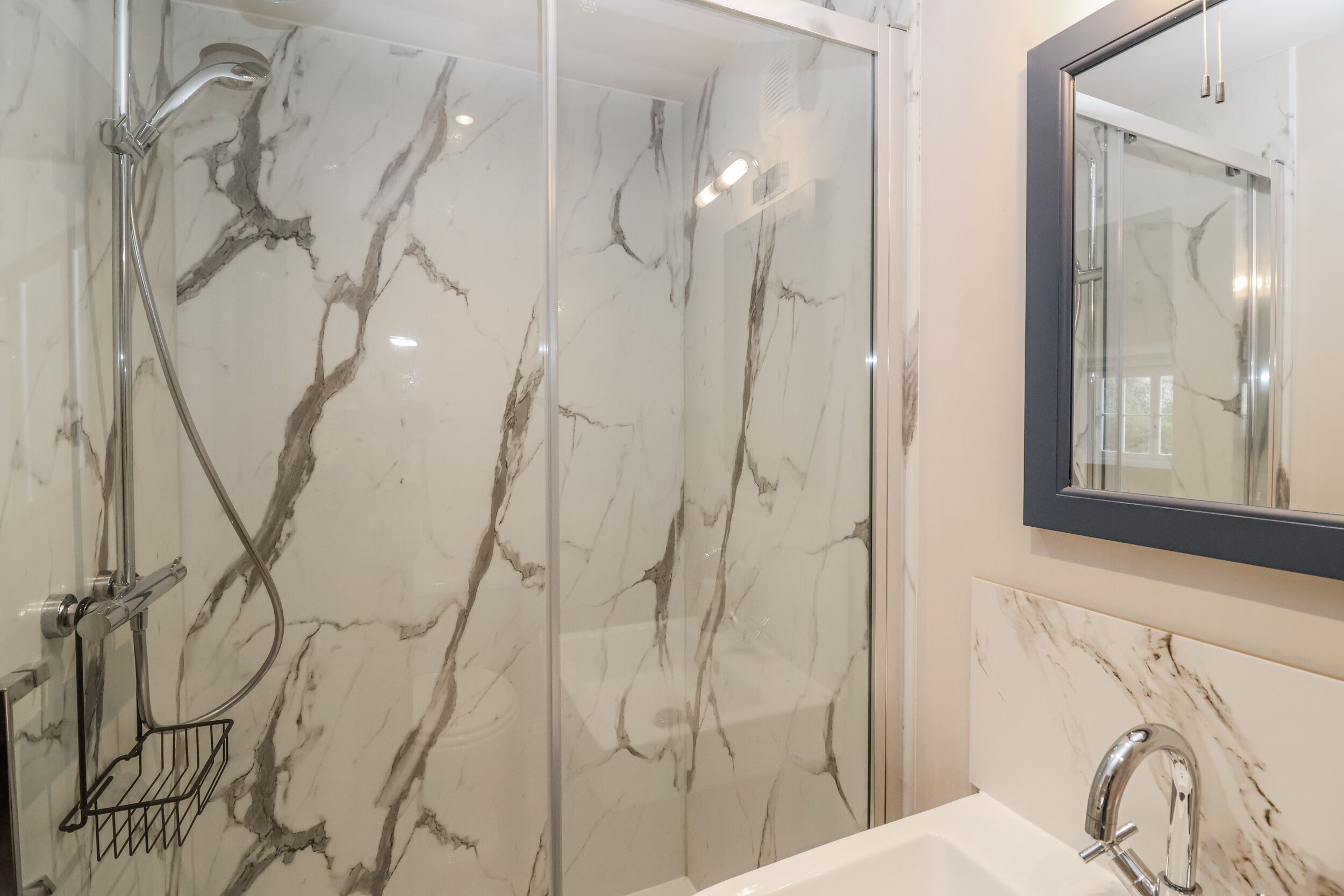 A bathroom with a glass-enclosed shower, a marble wall, a sink with a modern faucet, and a mirror above the sink.