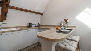 A kitchen with a wooden countertop, white cabinets, a sink, and a small dining area with stools. - The Old Dairy (Chippenham)