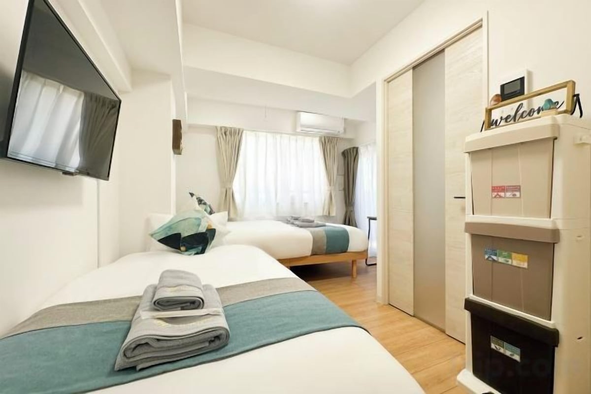 A hotel room with two beds, a flat-screen TV, a wardrobe, and a trash bin.