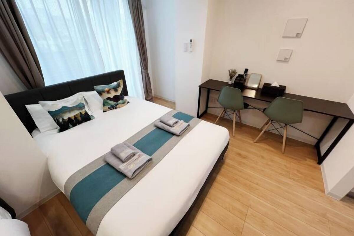 Een hotelkamer met een bed, een bureau, twee stoelen en een raam met gordijnen.