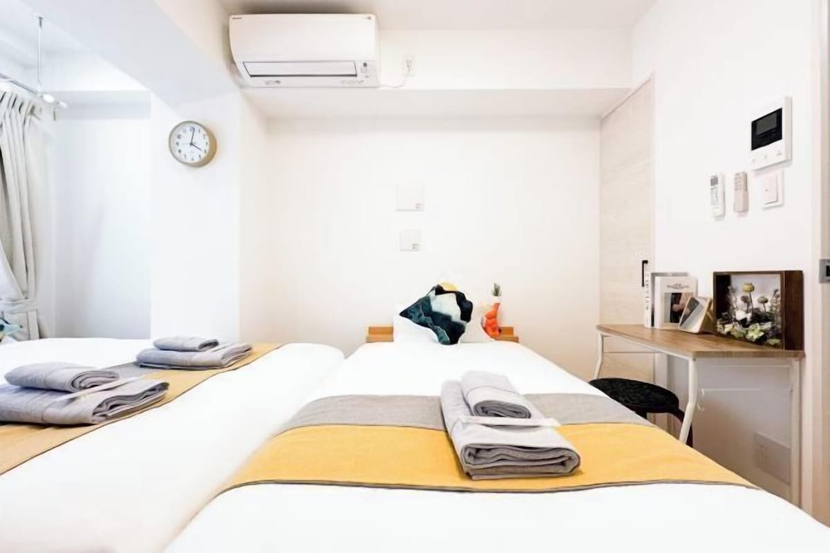 Habitación de hotel con dos camas, un escritorio, un reloj, aire acondicionado y un estante con objetos.
